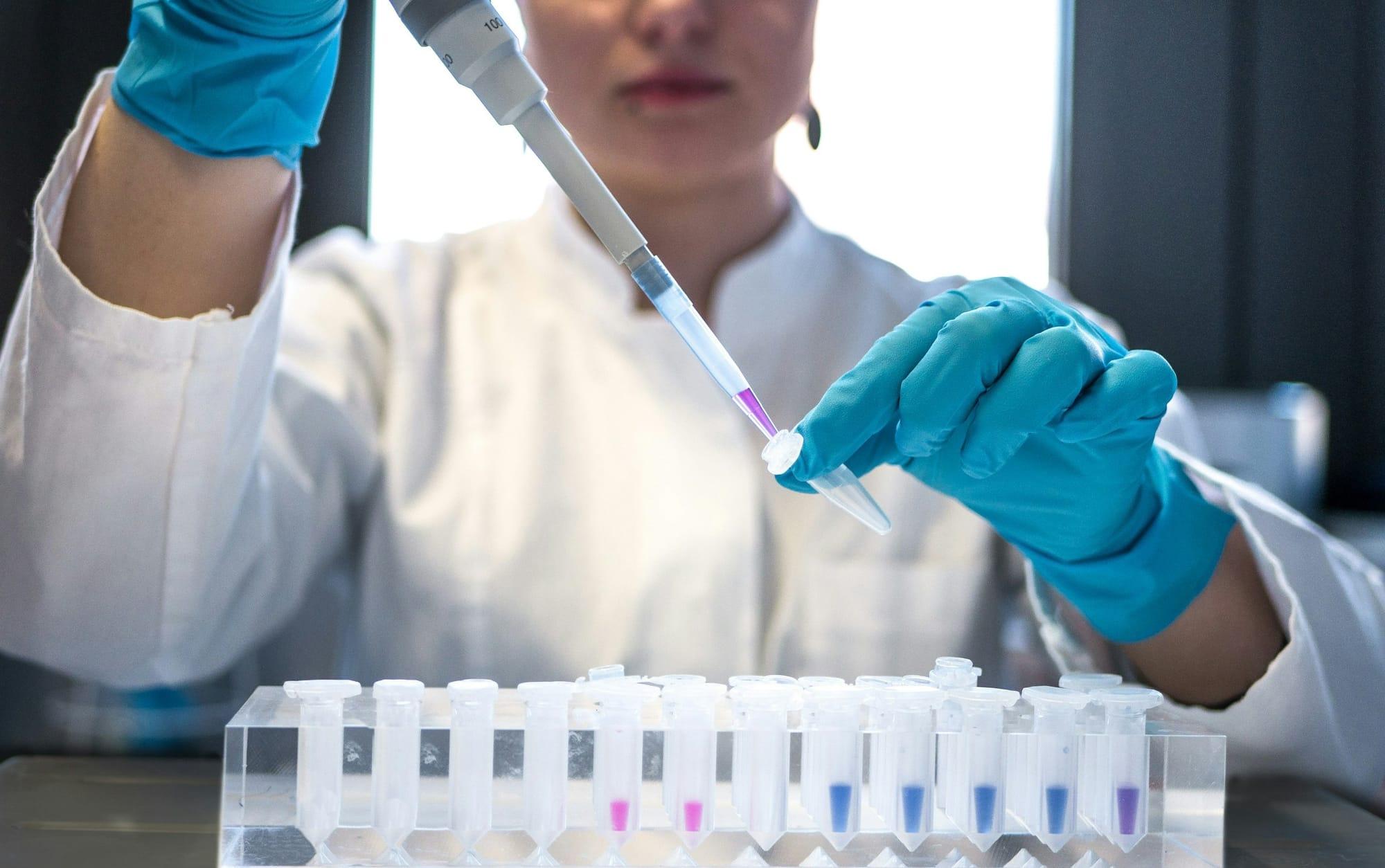 Scientist in gloves using a pipette over a row of test tubes