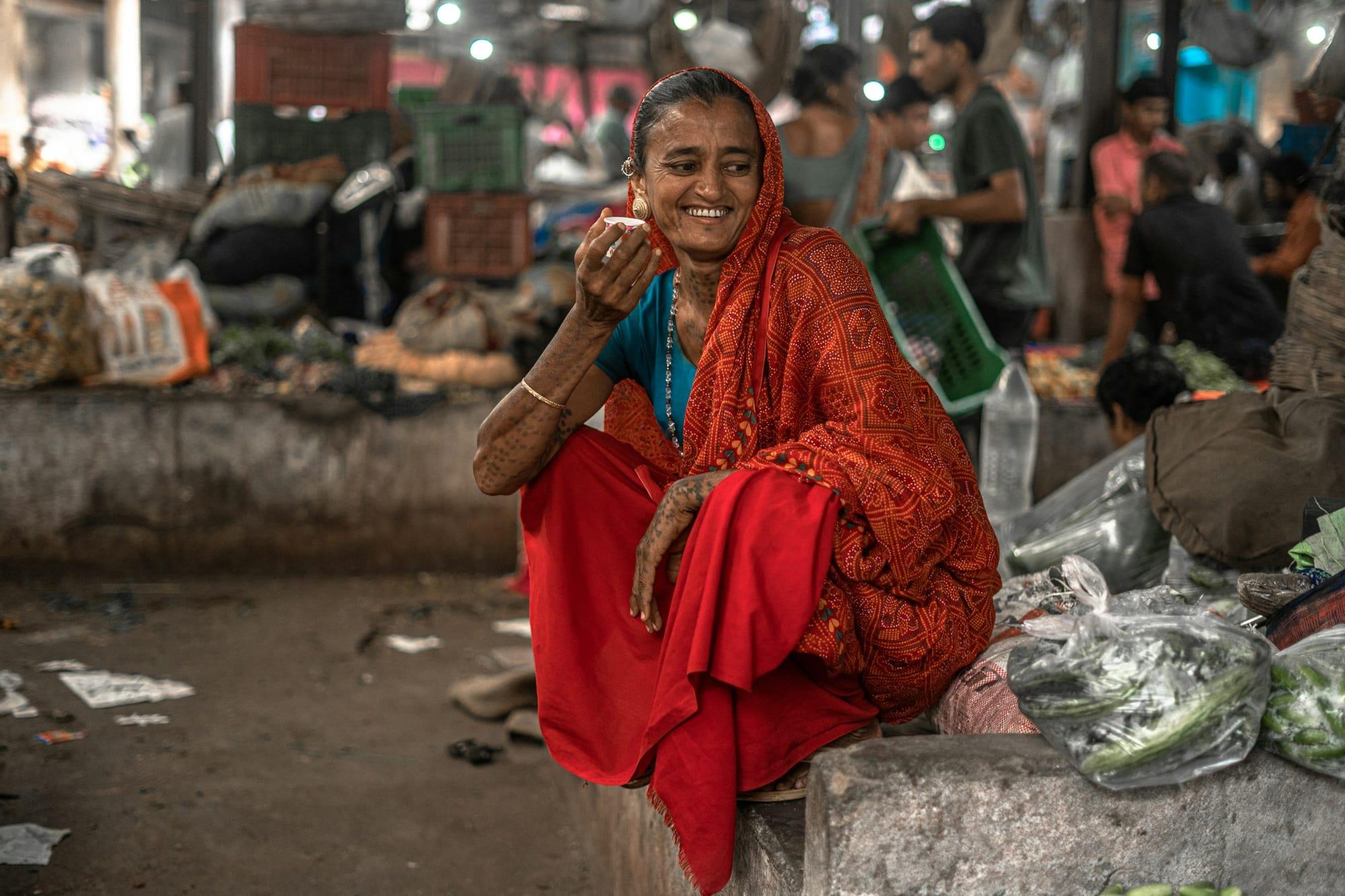 Woman in a red sari smiling while talking on her phone in a market
